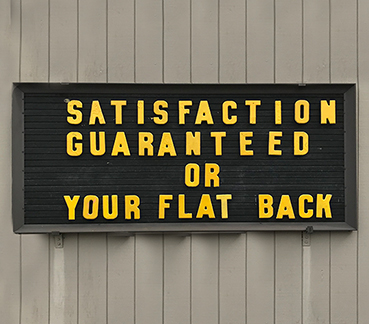 Outdoor sign with text: SATISFACTION GARANTEED OR YOUR FLAT BACK